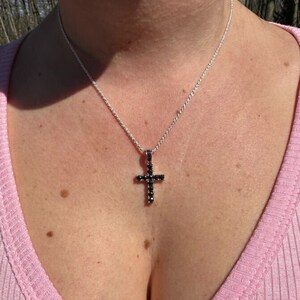 May include: A silver chain necklace with a black cross pendant. The cross is adorned with small black stones.