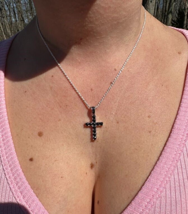 May include: A silver chain necklace with a black cross pendant. The cross is adorned with small black stones.