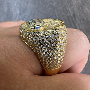 Puede incluir: Un anillo de oro con una piedra grande y facetada engastada en el centro. La piedra est&aacute; rodeada de diamantes m&aacute;s peque&ntilde;os, engastados en pav&eacute;. El anillo es una pieza llamativa y ser&iacute;a un gran regalo.