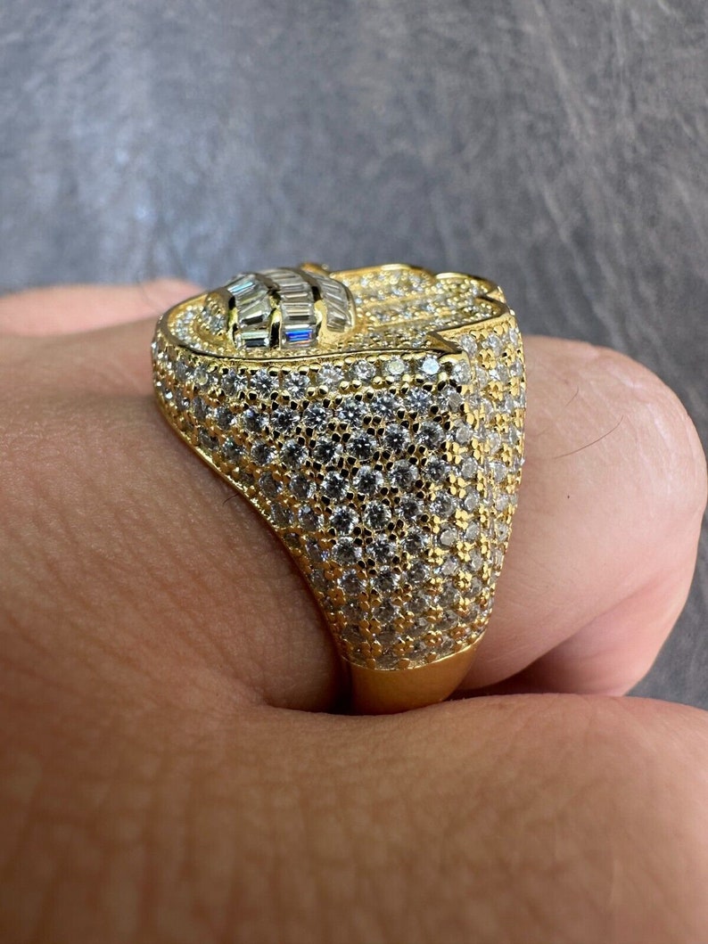 Puede incluir: Un anillo de oro con una piedra grande y facetada engastada en el centro. La piedra est&aacute; rodeada de diamantes m&aacute;s peque&ntilde;os, engastados en pav&eacute;. El anillo es una pieza llamativa y ser&iacute;a un gran regalo.