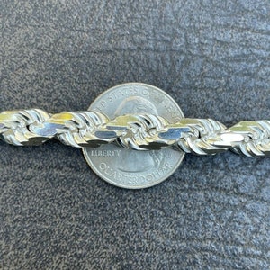 Puede incluir: Un collar de cadena de cuerda de plata con una moneda de veinticinco centavos de d&oacute;lar estadounidense como referencia de tama&ntilde;o. La cadena est&aacute; hecha de un dise&ntilde;o de cuerda trenzada gruesa.