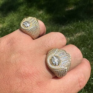 Puede incluir: Dos anillos de oro con un dise&ntilde;o de mano de Hamsa, engastados con diamantes baguette y redondos transparentes.