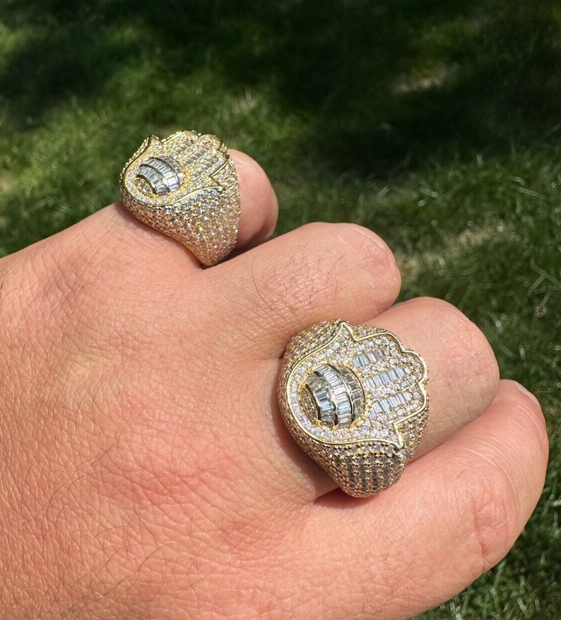 Puede incluir: Dos anillos de oro con un dise&ntilde;o de mano de Hamsa, engastados con diamantes baguette y redondos transparentes.