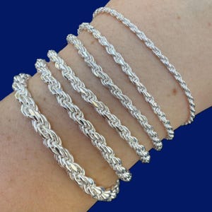 May include: A set of six silver rope chain bracelets of varying widths. The bracelets are arranged in order of size, with the smallest bracelet at the top and the largest bracelet at the bottom.