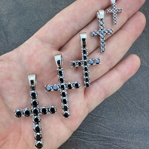 May include: Five silver cross pendants with black diamond accents. The crosses are of varying sizes, with the largest cross at the bottom of the image and the smallest cross at the top.