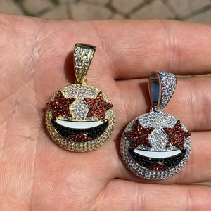 Puede incluir: Dos colgantes de oro y plata con un dise&ntilde;o de cara sonriente. Los ojos son estrellas rojas con piedras blancas y transparentes. La boca es negra y blanca.