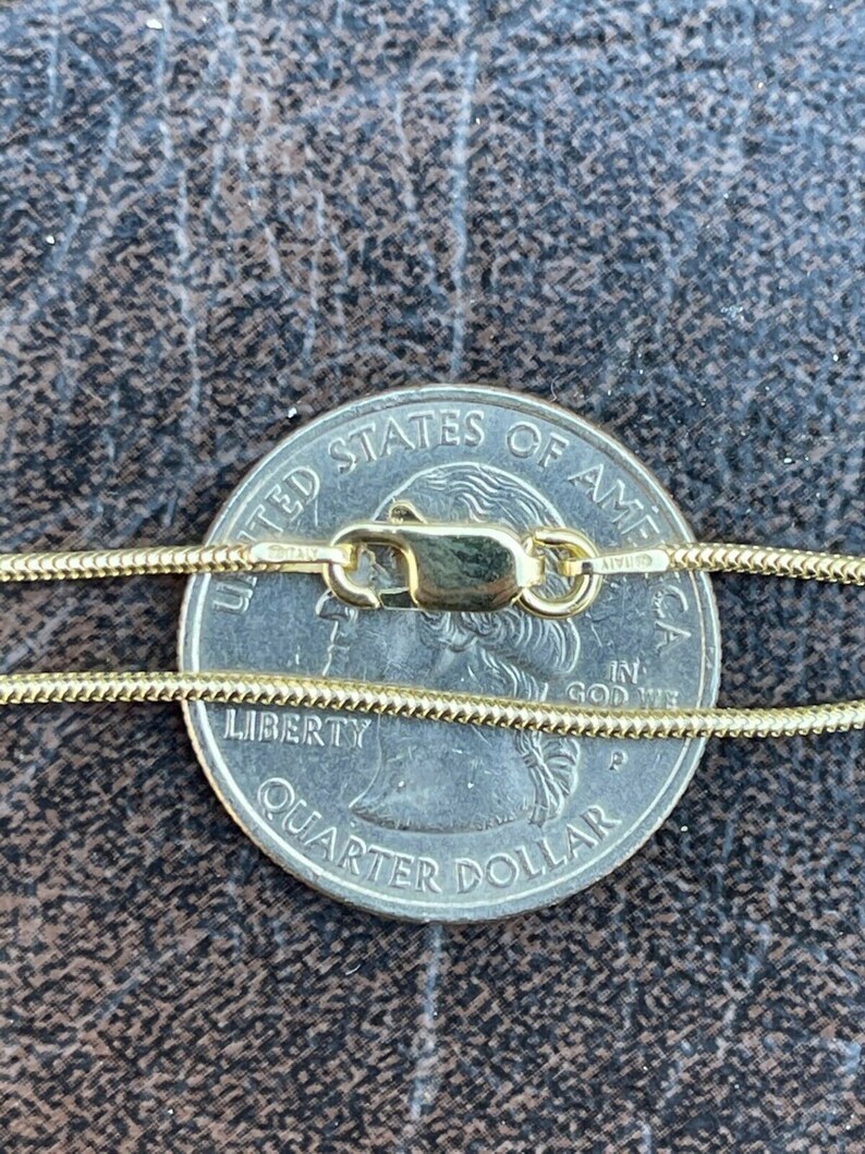 Puede incluir: Un collar de cadena de oro con un cierre de langosta, colocado sobre una moneda de 25 centavos de d&oacute;lar estadounidense. La moneda dice "United States of America" y "Liberty Quarter Dollar".