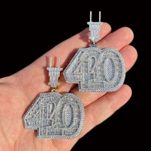 May include: Two silver-colored pendants, each displaying the number "40" in a bold, blocky font. The pendants are encrusted with small, sparkling stones, creating a dazzling effect. The pendants are held up by a small, rectangular bail.