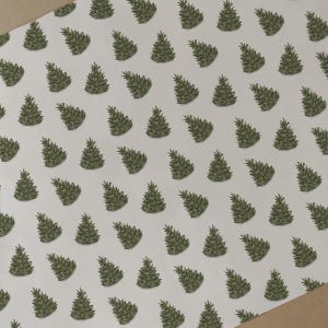 May include: White wrapping paper featuring a repeating pattern of green Christmas trees. The trees are depicted in a simple, hand-drawn style. A brown edge of the paper is visible in the corner.