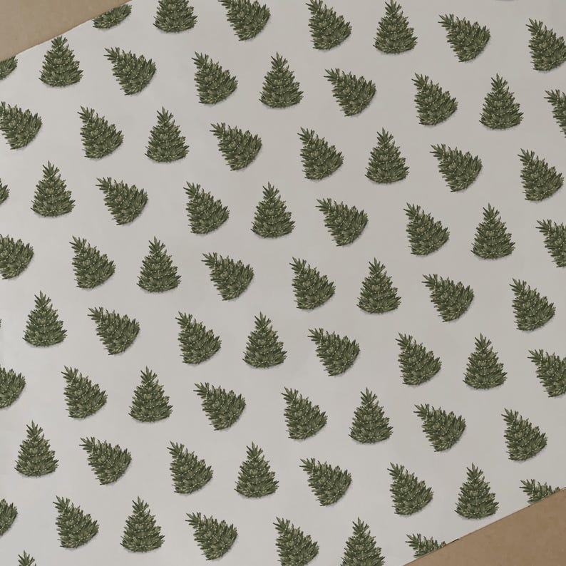 May include: White wrapping paper featuring a repeating pattern of green Christmas trees. The trees are depicted in a simple, hand-drawn style. A brown edge of the paper is visible in the corner.