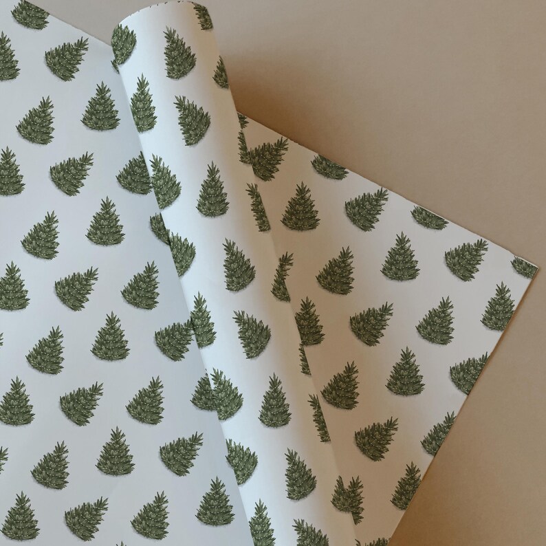 May include: White wrapping paper featuring a repeating pattern of green Christmas trees. The paper is partially rolled, showing the pattern on both sides. The trees have dark green outlines and shading.