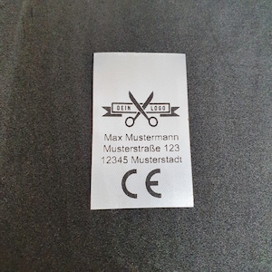 Könnte beinhalten: Ein weißes Etikett mit schwarzem Text und einem Logo. Das Logo ist eine Schere mit den Worten "DEIN LOGO" auf einem Band. Der Text lautet "Max Mustermann Musterstraße 123 12345 Musterstadt CE".