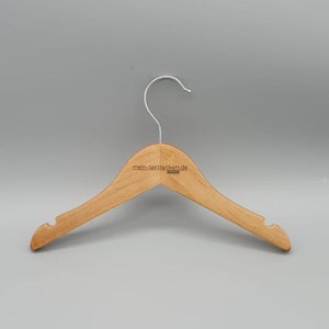 May include: A wooden clothes hanger with a silver hook. The hanger has a rounded shape and is made of natural wood. The text "mein-textilletikett.de" is printed on the hanger.