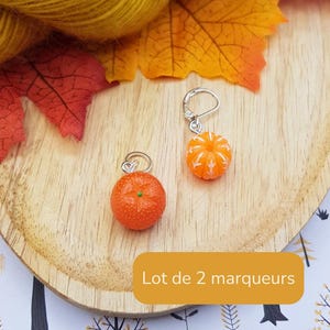 Op de afbeelding: Twee steekmarkeerders met oranje fruitbedels en zilverkleurige metalen ringetjes. De ene bedel is een textuurrijke sinaasappel met een groen midden, de andere is een gesegmenteerd sinaasappelpartje met witte details. Tekst: Lot de 2 marqueurs.