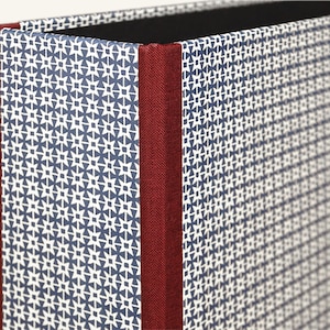 May include: Close-up of a blue and white patterned storage box with a red fabric spine.
