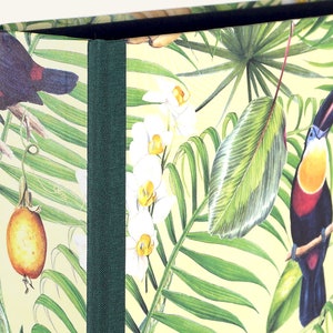 Könnte beinhalten: Eine grüne und gelbe Box mit einem tropischen Druck mit Tukanen, Orchideen und Palmenblättern. Die Box hat einen grünen Stoffrücken.