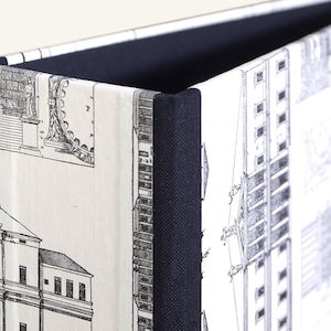 Può includere: Una scatola con un motivo bianco e nero con una spina in tessuto nero. Il motivo presenta disegni architettonici di edifici.