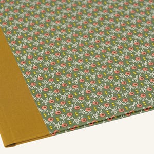 Könnte beinhalten: Ein Notizbuch mit einem senfgelben Rücken und einem gemusterten Einband. Der Einband zeigt ein sich wiederholendes Blumenmuster in Weiß, Rosa und Gelb auf grünem Hintergrund. Das Notizbuch ist geöffnet.