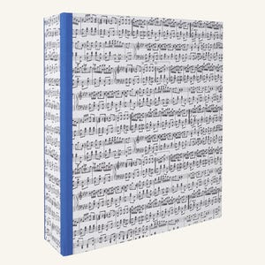 May include: A rectangular notebook with a blue spine and covers covered in musical notes. The musical notes are printed in black on a white background. The notebook is standing upright.