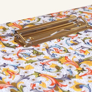 Könnte beinhalten: Eine Klemmbrett mit einem floralen Muster in Rot-, Blau-, Gelb- und Grüntönen. Das Klemmbrett hat einen silbernen Metallclip.