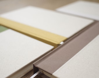 May include: Four notebooks with different colored covers. The covers are beige, yellow, green, and brown. The notebooks are stacked on top of each other.