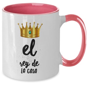 Puede incluir: Taza de cer&aacute;mica blanca con interior y asa rosa. La taza presenta un dise&ntilde;o de corona dorada con una gema verde y el texto en espa&ntilde;ol "el rey de LA CASA" en letras negras.