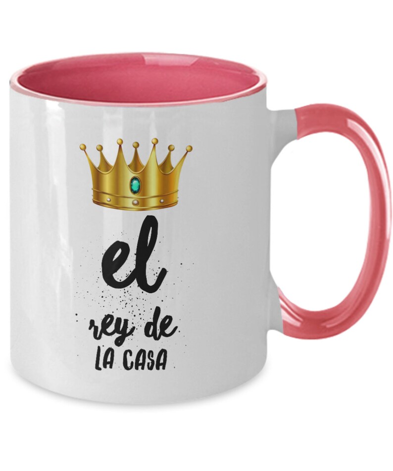 Puede incluir: Taza de cer&aacute;mica blanca con interior y asa rosa. La taza presenta un dise&ntilde;o de corona dorada con una gema verde y el texto en espa&ntilde;ol "el rey de LA CASA" en letras negras.