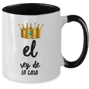 Puede incluir: Taza de cer&aacute;mica blanca con interior y asa negros. La taza presenta un dise&ntilde;o de corona dorada con una gema verde y el texto "el rey de LA CASA" en escritura negra.