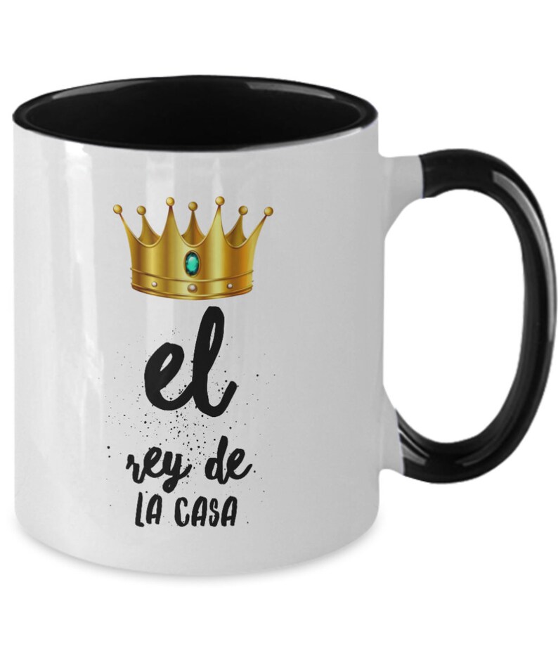 Puede incluir: Taza de cer&aacute;mica blanca con interior y asa negros. La taza presenta un dise&ntilde;o de corona dorada con una gema verde y el texto "el rey de LA CASA" en escritura negra.