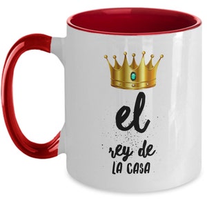 Puede incluir: Taza de cer&aacute;mica blanca con interior y asa rojos. La taza presenta una corona dorada con una gema verde y el texto "el rey de la casa" en escritura negra.