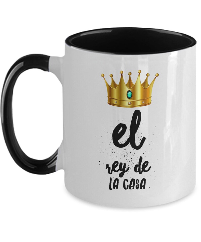 Puede incluir: Taza de cer&aacute;mica blanca con interior y asa negros. La taza presenta una corona dorada con una gema verde y el texto en espa&ntilde;ol "el rey de la casa" en escritura negra.