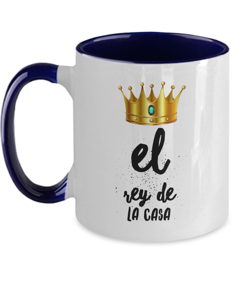 Puede incluir: Taza de cer&aacute;mica blanca con interior y asa azul marino. La taza presenta una corona dorada con una gema verde y el texto "el rey de LA CASA" en escritura negra.