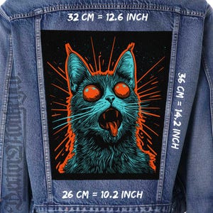 Pode incluir: Um gato preto e azul com olhos vermelhos brilhantes e a língua de fora. O gato está rodeado por raios de luz laranja e vermelho. A imagem está em uma jaqueta de jeans com medidas em polegadas e centímetros.