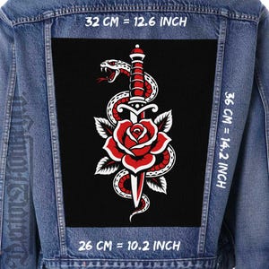 May include: A blue denim jacket featuring a large rectangular back patch with a black background. The patch displays a white snake coiled around a silver dagger piercing a red rose. Text indicates dimensions of 12.6 inches by 14.2 inches by 10.2 inches.