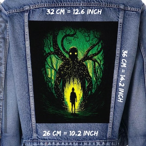 Könnte beinhalten: Ein schwarzer und grüner Grafik-Patch mit einer schattenhaften Figur mit leuchtenden Augen, die in einem dunklen Wald steht. Der Patch ist 32 cm breit, 36 cm hoch und 26 cm tief.