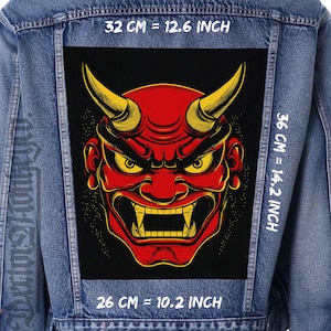 Peut inclure: Veste en jean avec un grand patch rectangulaire représentant un visage de démon rouge avec des cornes et des yeux jaunes. Le patch mesure 32 cm sur 36 cm et 26 cm. Le texte "32 CM = 12.6 INCH", "36 CM = 14.2 INCH", et "26 CM = 10.2 INCH" est visible.