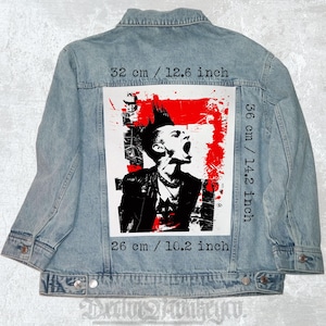 Peut inclure: Veste en jean bleu clair avec un grand motif au dos. Le motif présente une illustration en noir et blanc d'une personne criant avec une crête, sur un fond rouge éclaboussé. Le motif mesure 32 cm de large sur 36 cm de haut.