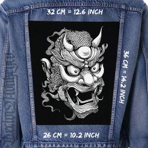 Peut inclure: Veste en jean avec un grand patch noir orné d'une illustration détaillée en noir et blanc d'un visage de démon japonais. Le patch mesure 32 cm de large, 36 cm de haut et 26 cm de long.