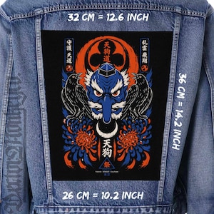 Könnte beinhalten: Eine blaue Jeansjacke mit einem großen rechteckigen Rückenaufnäher, der eine blaue Tengu-Maske, zwei schwarze Krähen und orangefarbene Chrysanthemen zeigt. Der Aufnäher enthält japanischen Text und misst 32 cm mal 36 cm mal 26 cm.