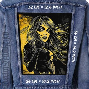May include: A black and yellow graphic patch of a woman with long hair, wearing a black leather jacket and a black mask. The patch is sewn onto a blue denim jacket. The text "32 CM = 12.6 INCH", "36 CM = 14.2 INCH", and "26 CM = 10.2 INCH" is printed on the denim jacket.