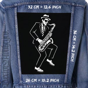 Op de afbeelding: Spijkerjasje met een zwart embleem met een witte illustratie van een saxofonist. De patch is 32 cm breed, 36 cm hoog en 26 cm lang. De tekst "32 CM = 12.6 INCH", "36 CM = 14.2 INCH" en "26 CM = 10.2 INCH" zijn zichtbaar.