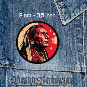 May include: A round patch featuring a Native American profile in red and black, set against a red and tan background. The patch measures 3.5 inches (9 cm) in diameter. The image is set against a denim background.