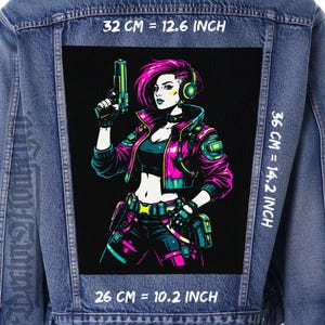 Peut inclure: Veste en jean avec un grand patch rectangulaire représentant un personnage féminin futuriste aux cheveux roses, avec un casque et un pistolet. Le patch mesure 32 cm de large, 36 cm de haut et 26 cm de long. Le personnage porte un haut et un pantalon noirs avec une veste rose et turquoise.