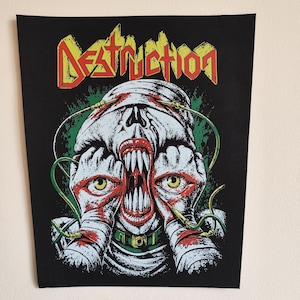 May include: A black fabric patch featuring the word DESTRUCTION in yellow and red letters at the top. Below, a graphic illustration shows a bandaged, monstrous figure with sharp teeth, yellow eyes, and green wires connected to its head.