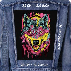 Puede incluir: Chaqueta vaquera con un parche rectangular grande con un diseño de lobo colorido. La cara del lobo está representada en vibrantes tonos rosa, amarillo y turquesa, con efectos de pintura goteando. El parche mide 32 cm por 36 cm.