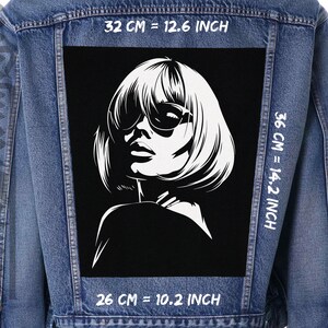 May include: A black and white illustration of a woman with short hair wearing sunglasses. The image is printed on a denim jacket with white text that reads "32 CM = 12.6 INCH", "36 CM = 14.2 INCH", and "26 CM = 10.2 INCH".