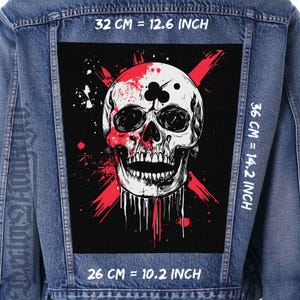 May include: A denim jacket with a large, black patch featuring a detailed skull design. The skull is white with red accents and a black club symbol. The patch measures 32 cm by 36 cm and 26 cm.