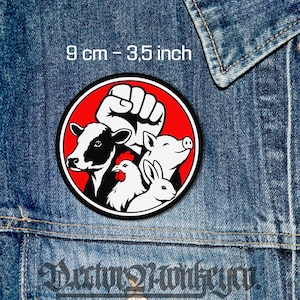 May include: A round patch with a red background and a black border. The patch features a white fist, a cow, a pig, a chicken, and a rabbit. The text "9 cm - 3.5 inch" is at the top.