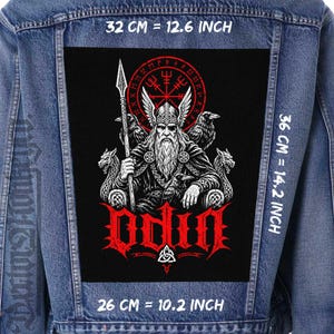 May include: A blue denim jacket featuring a large rectangular black patch on the back. The patch displays a bearded figure in a winged helmet holding a spear, flanked by ravens and wolves, with the red text ODIN. Dimensions are 12.6 by 14.2 inches.