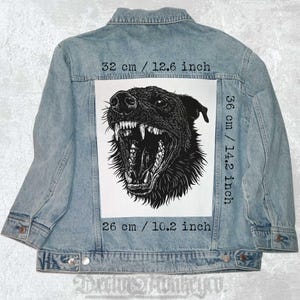 May include: A black and white illustration of a snarling dog's head on a white background. The image is on a denim jacket with measurements in inches and centimeters.